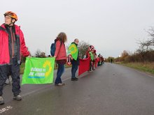 Auf dem Bild sind mehrere rot gekleidete Personen zu sehen, welche mit Fahnen von Bündnis90/Die Grünen zwischen sich eine Linie bilden.