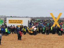 Hundererte Klimademonstrant*innen in Lützerath, die ein großes gelbes X hochalten.