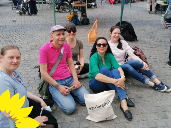 !B 6 bFrauen und Männer sitzen auf dem Marktplatz vor ihnen steht ein Beutel mit der Aufschrift "Barrierefreiheit"