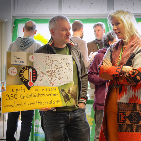 Ein männliches Mitglied hält ein Schild in der Hand, in der Hand, auf dem die Erhitzung der Stadt und der Verlust der Bäume, thematisiert wird. Neben ihm steht Katharina Krefft.