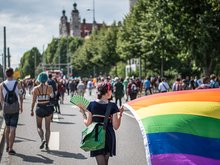 Auf dem Foto ist eine Menschenmenge zu sehen (von hinten) welche vor dem unscharfen Hintergrund, dem Leipziger neuen Rathaus, mit Regenbogenfahnen und bunten Luftballons demonstriert.