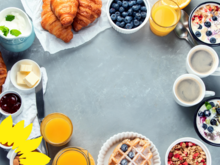 !B Frühstückstisch mit Kaffeetassen, Saft, Tellern und Schüsseln mit Beeren, Müsli, Croissants, Obstsalat