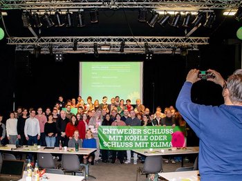 Es ist ein Gruppenfoto zu sehen. Die Personen in der ersten Reige tragen ein Banner mit der Aufschrift: Entweder Schluss mit Kohle oder Schluss mit Klima.