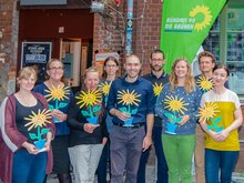 Auf dem Bild stehen neun Personen mit einer Holzsonnenblume in der Hand vor dem Eingang der Halle D des Werk 2 in Leipzig.