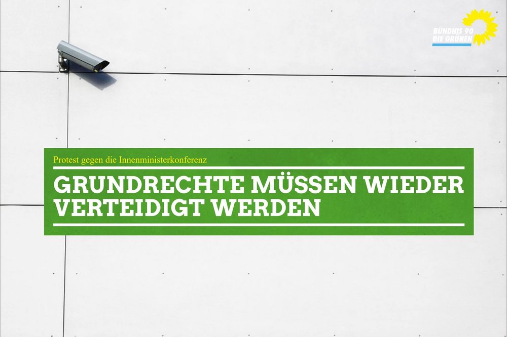 Auf dem Foto ist eine Häuserwand zu sehen mit einer angebrachten Überwachungskamera. Mittig ist ein grüner Kasten zu sehen in welchem folgender Schriftzug steht: "Grundrechte müssen wieder verteidigt werden."